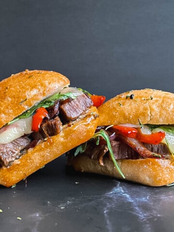 Side view of steak sandwich with arugula, caramelized onion and pepper, and gruyere cheese.