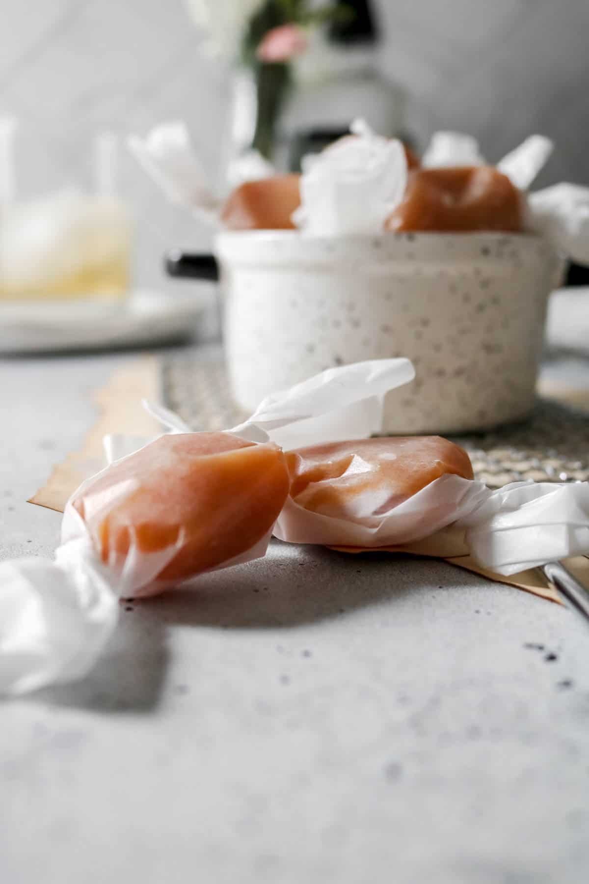 Side view of whiskey salted caramels in a dish and wrapped in wax paper.