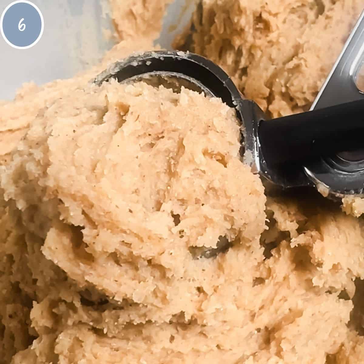 Scooping cookie dough out of bowl to roll it and place it on cookie sheet.