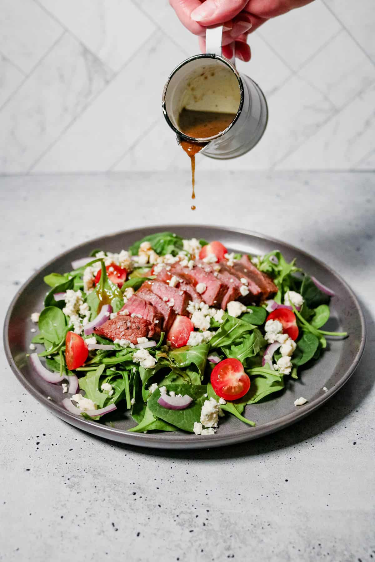 Balsamic dressing being poured onto arugula spinach steak salad.