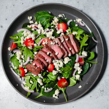 Overhead view of spinach arugula steak salad with tomatoes, red onion, and gorgonzola cheese.