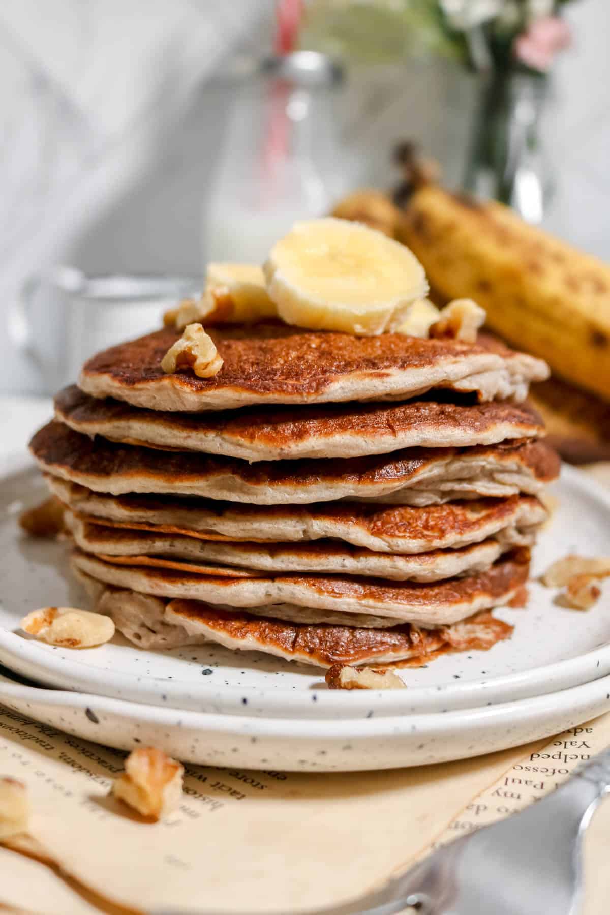 Stack of sourdough banana nut pancakes with banana slices and chopped pecans on top.