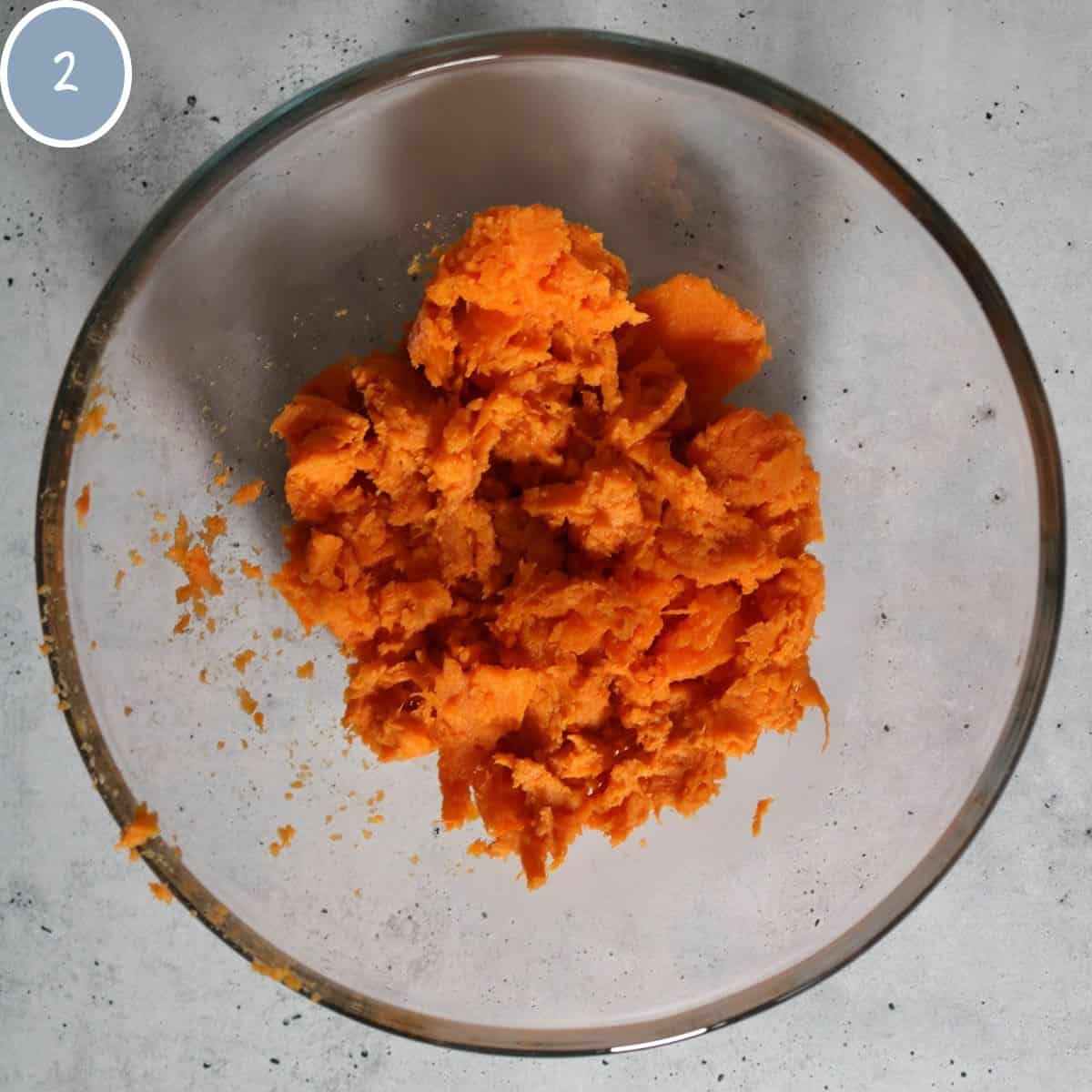 Cooked sweet potato mashed up in a glass bowl.