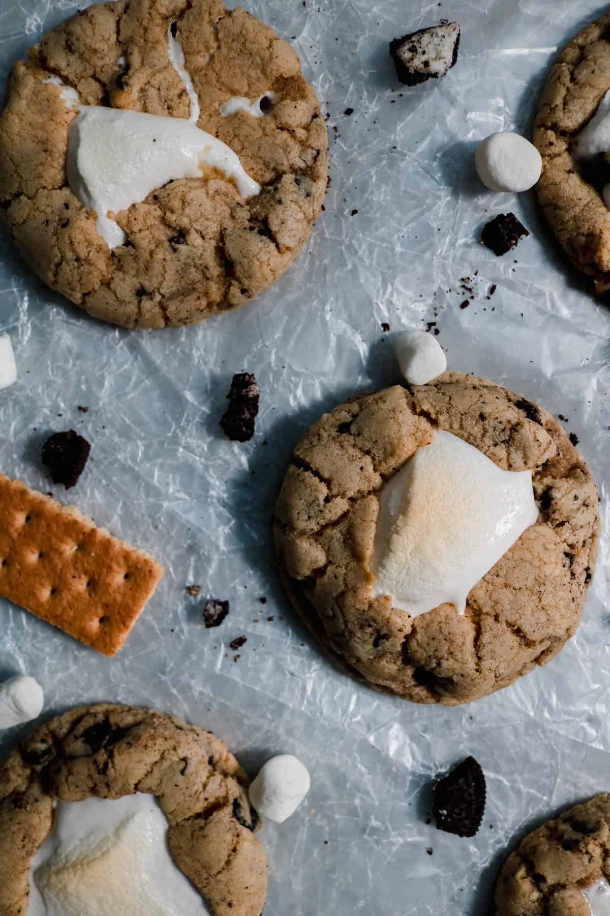 S'moreo cookies on parchment paper surrounded by mini marshmallows and Oreo bits.