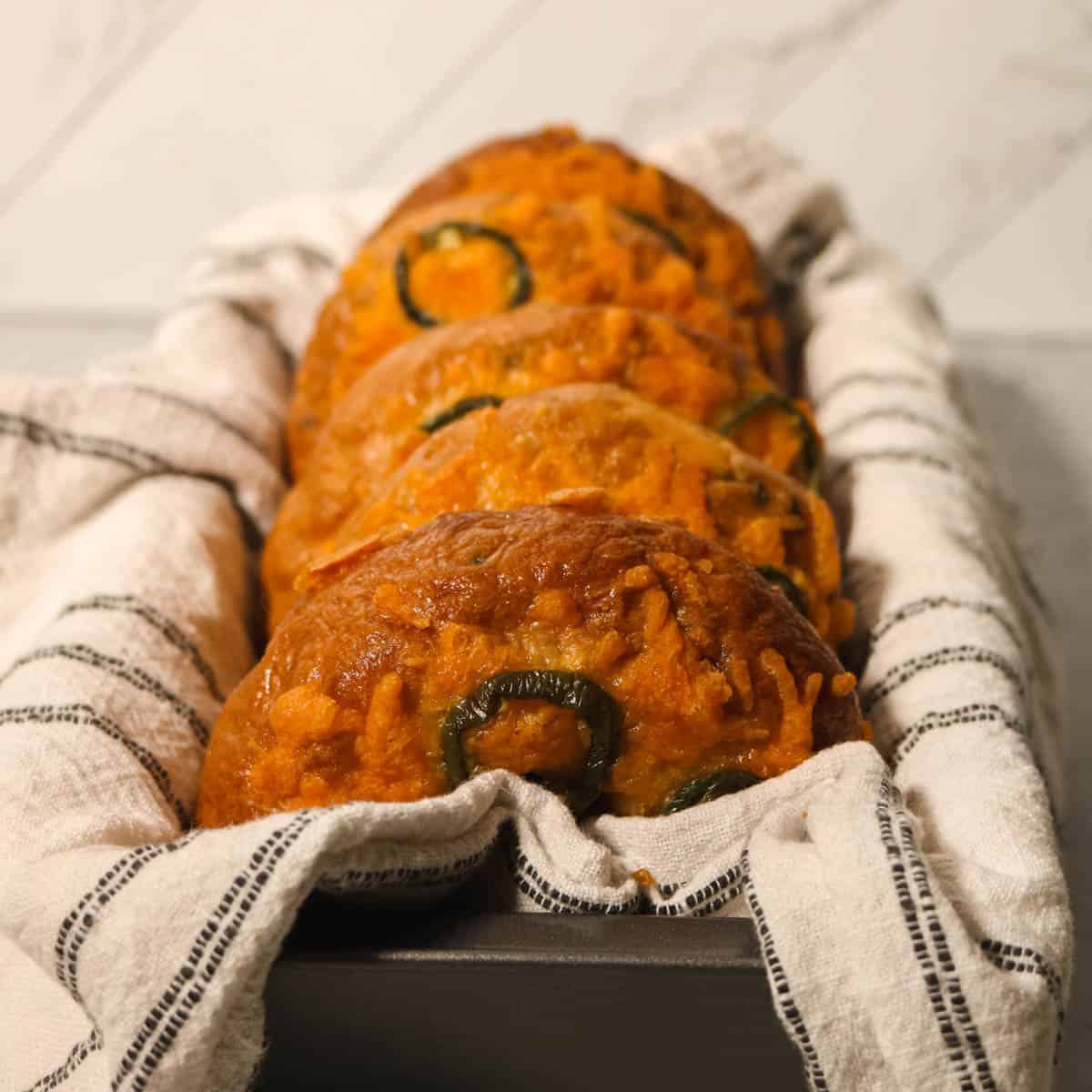 Side view of bagels in a bread pan with a white dish towel.