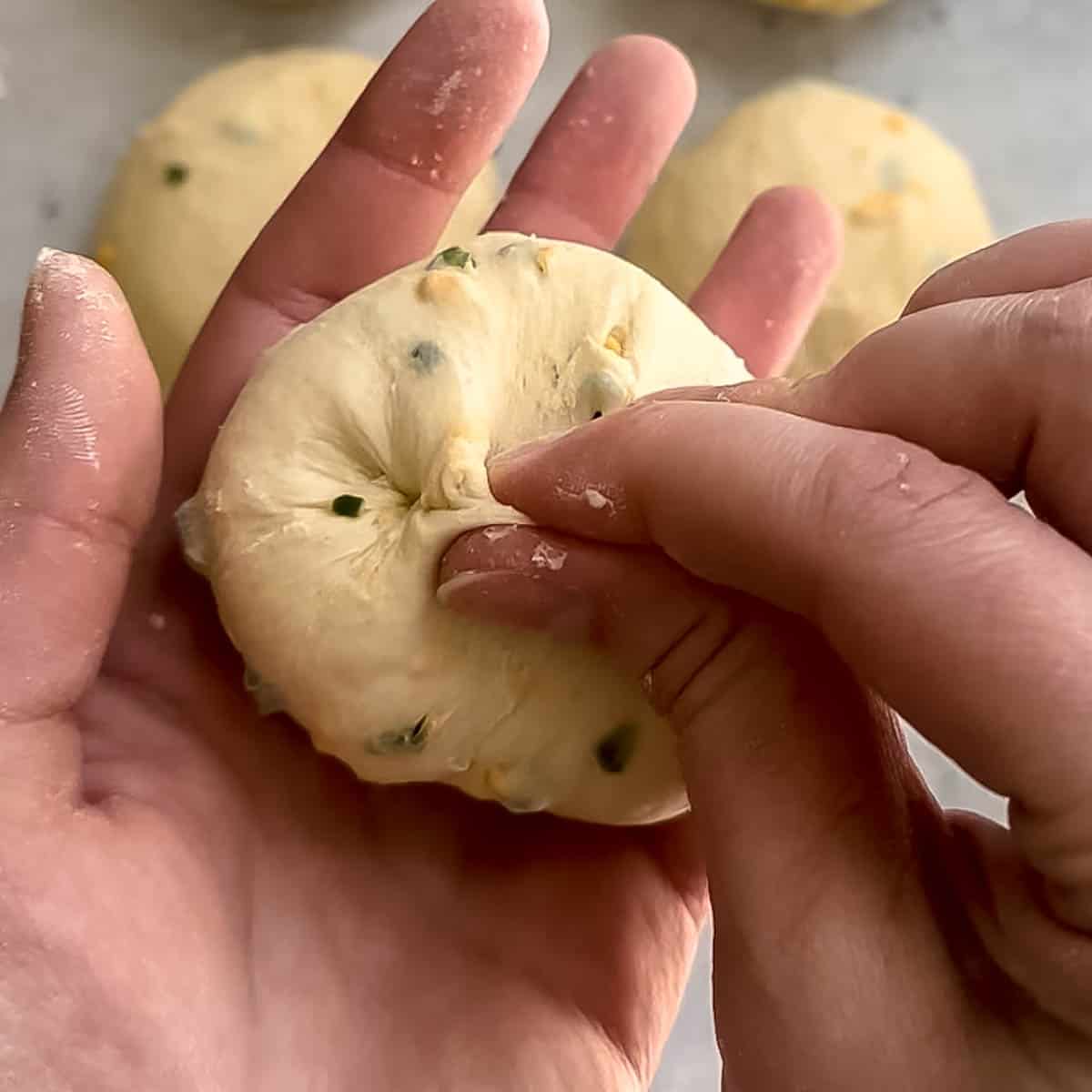 Pinching the bottom seams of the bagel dough to shape it into a ball.