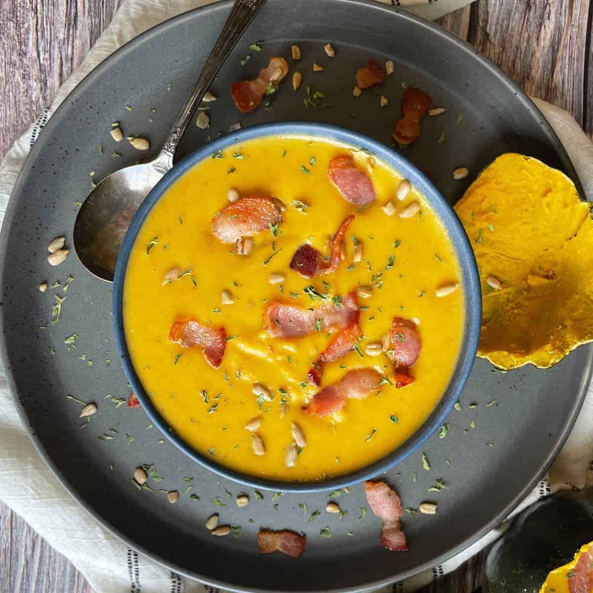 Overhead view of acorn squash soup with bacon, sunflower seeds, parsley on top.