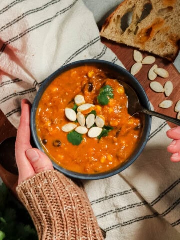 Overhead view of pumpkin chorizo soup with someone taking a spoonful.