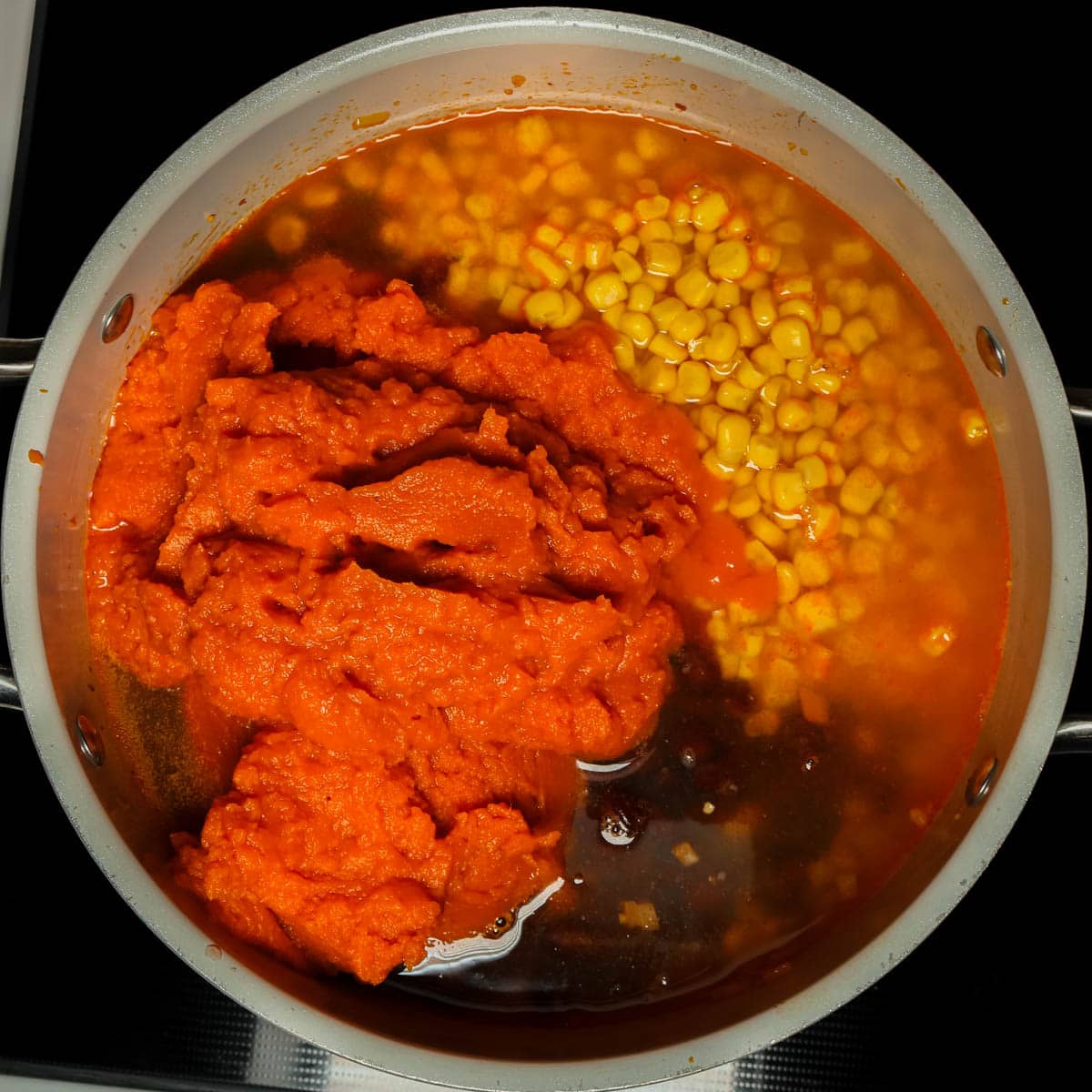 Pumpkin, broth, and vegetables being added a pot to make pumpkin chorizo soup.