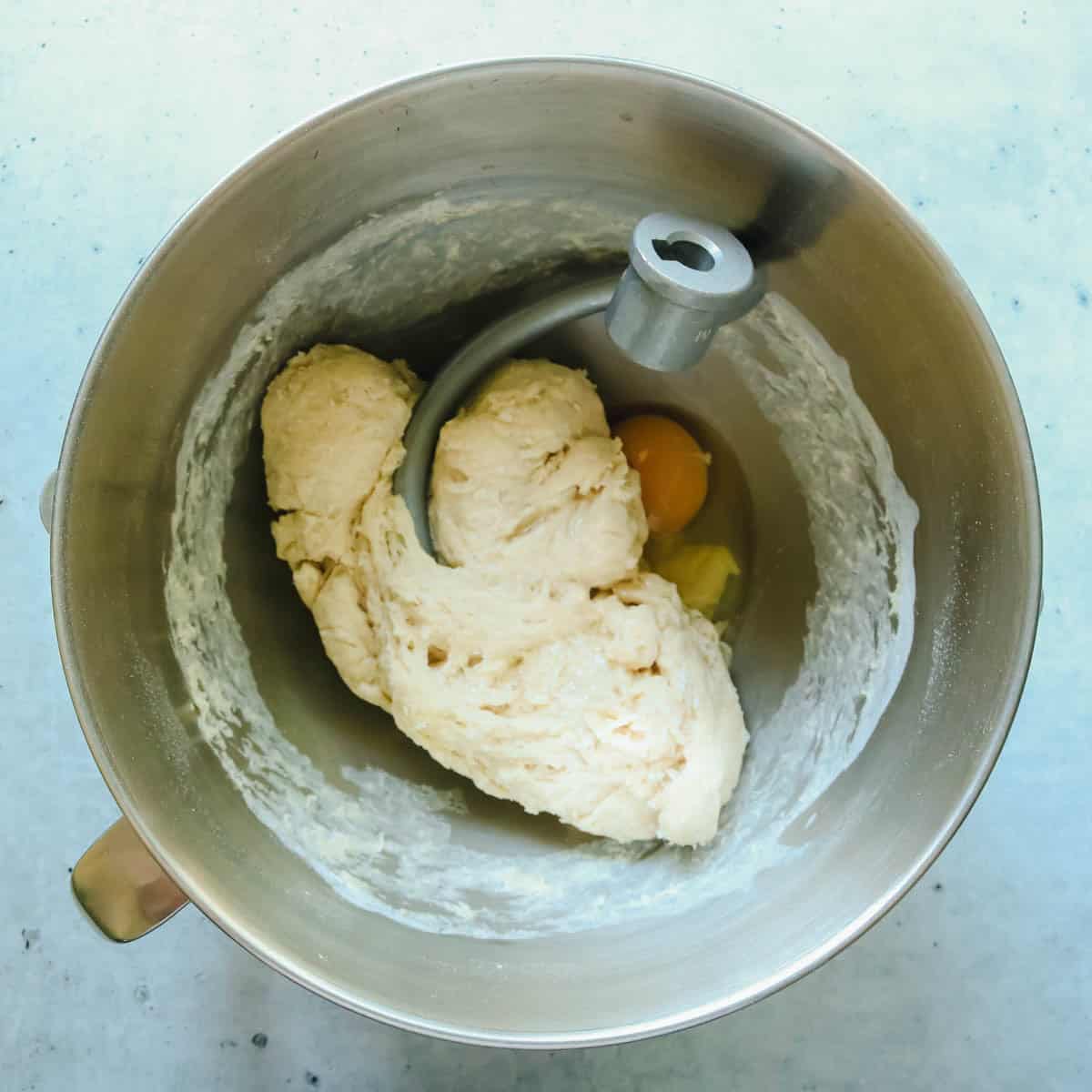 Egg being added to the dough in a mixing bowl.