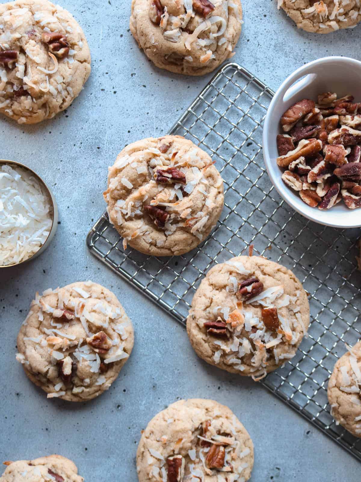 Overhead view of coconut pecan cookies on a cooling rack with small bowls of shredded coconut and chopped pecans.