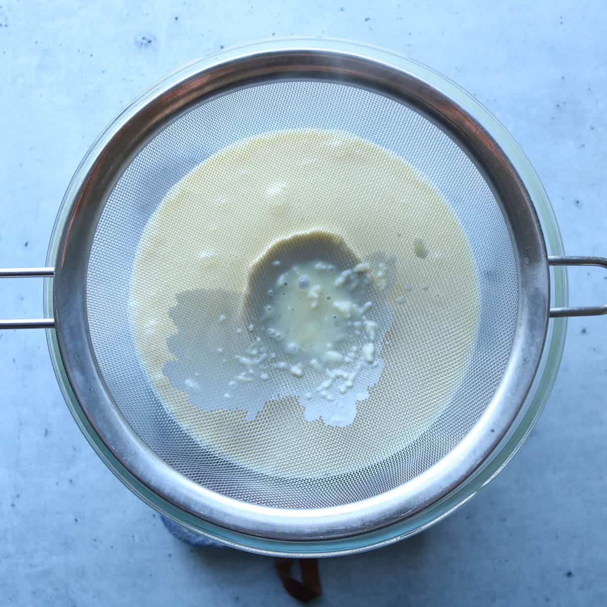 Ice cream mixture being ran through a fine mesh strainer.