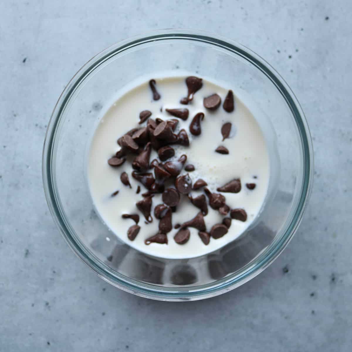 Chocolate chips and heavy cream in a bowl before being heated to make chocolate ganache.