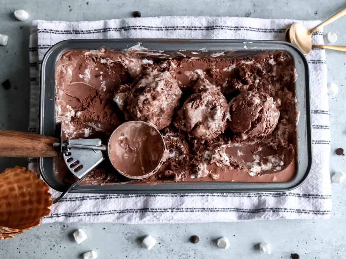 Overhead view of chocolate marshmallow ice cream in a bread pan with scoops taken out of it.