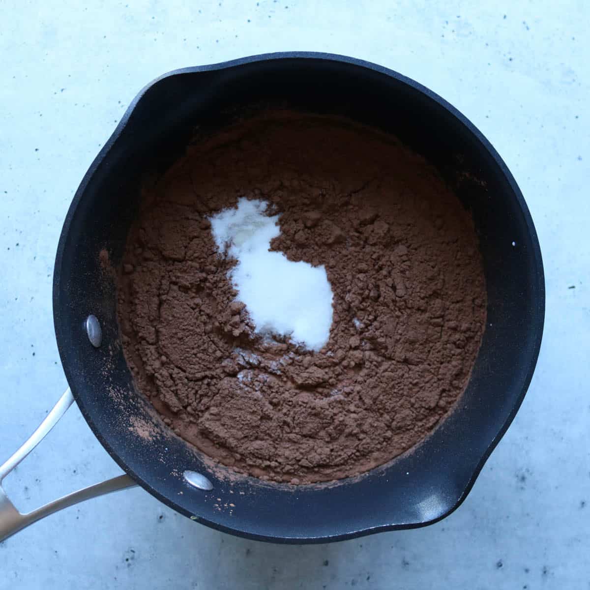 Heavy cream, milk, cocoa powder, and sugar in a saucepan before being cooked on stove top.