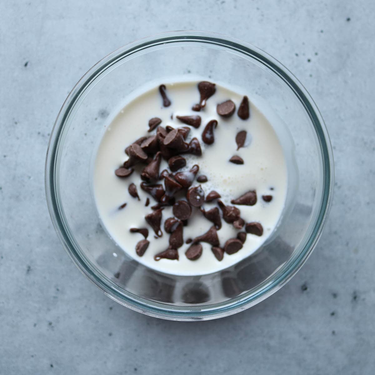 Chocolate chips and heavy cream in a glass bowl.